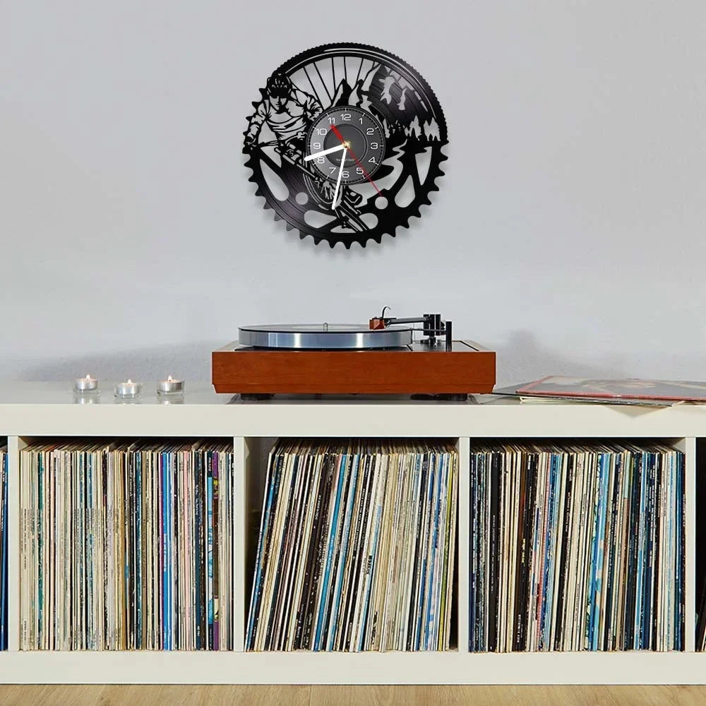 Mountain bike vinyl record wall clock featuring intricate laser-cut MTB design with detailed cyclist silhouette and bike components on black vinyl record. Clock presented in room setting near vinyl record player and record collection.